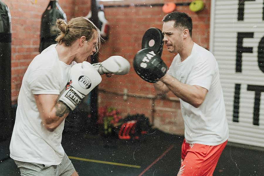 Two people practicing boxing with practice pads and gloves