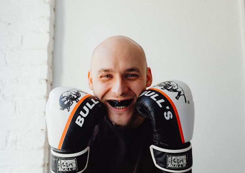 A man holding boxing gloves, smiling around a mouth guard