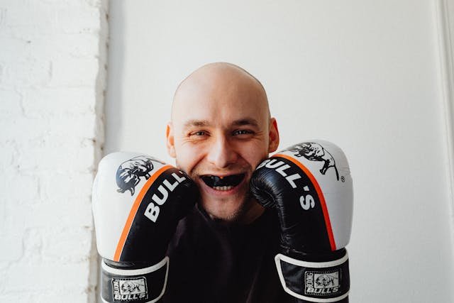 A smiling man wearing boxing gloves and a mouthguard