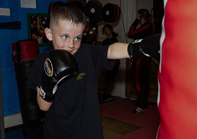 A young boy smiling whilst punching a training bag